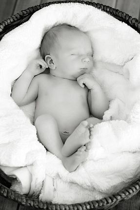 A black and white photo of a newborn baby sleeping in a basket.