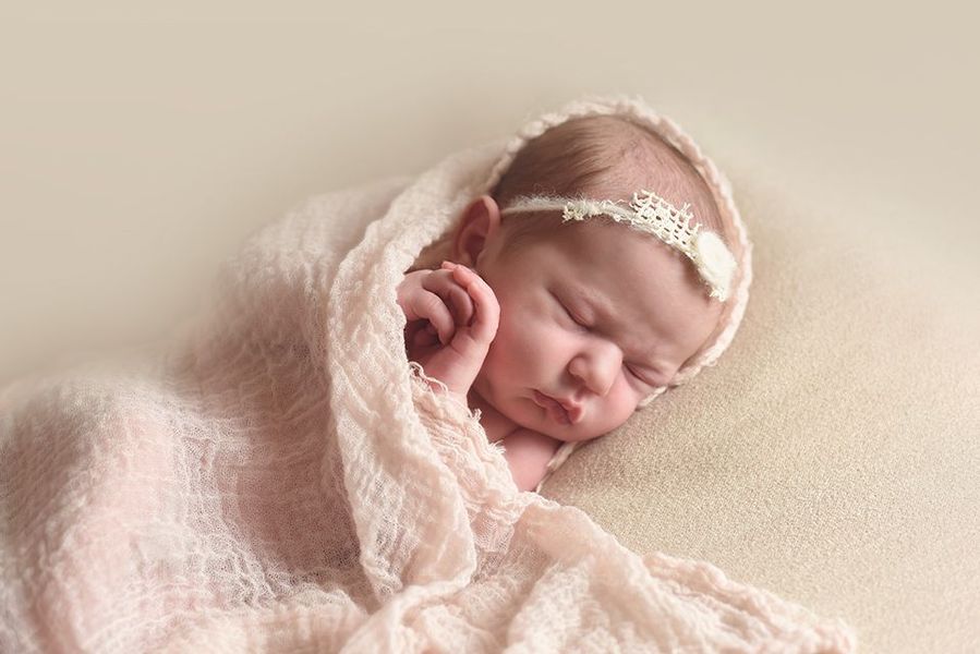 A newborn baby is wrapped in a pink blanket and wearing a headband.