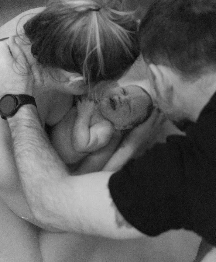 A black and white photo of a man and woman holding a newborn baby.