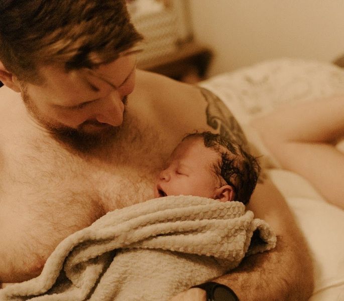 A man is holding a newborn baby wrapped in a towel.