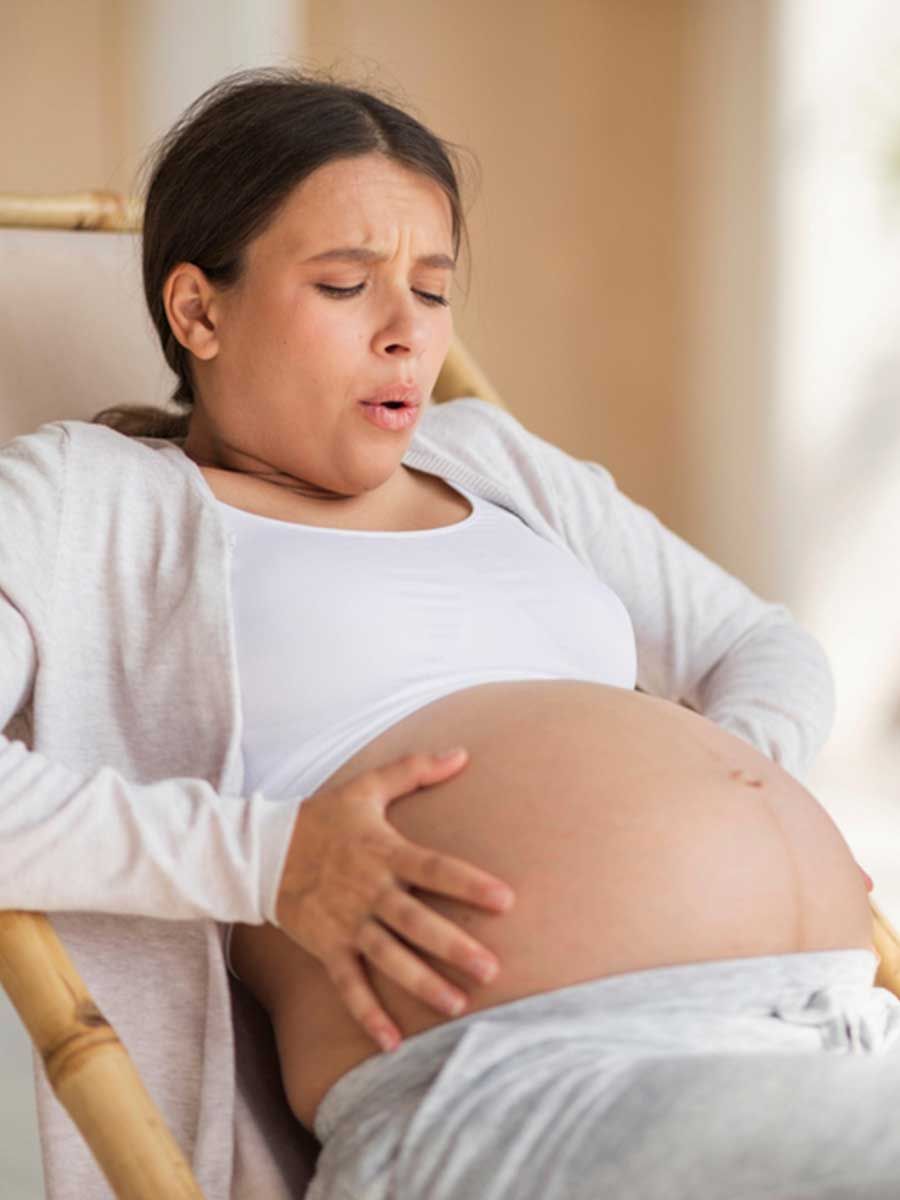 A pregnant woman is sitting in a chair holding her belly.