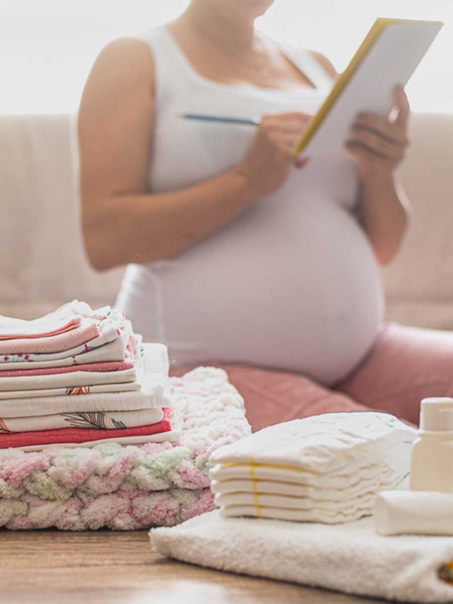 A pregnant woman is sitting on a couch looking at a clipboard.