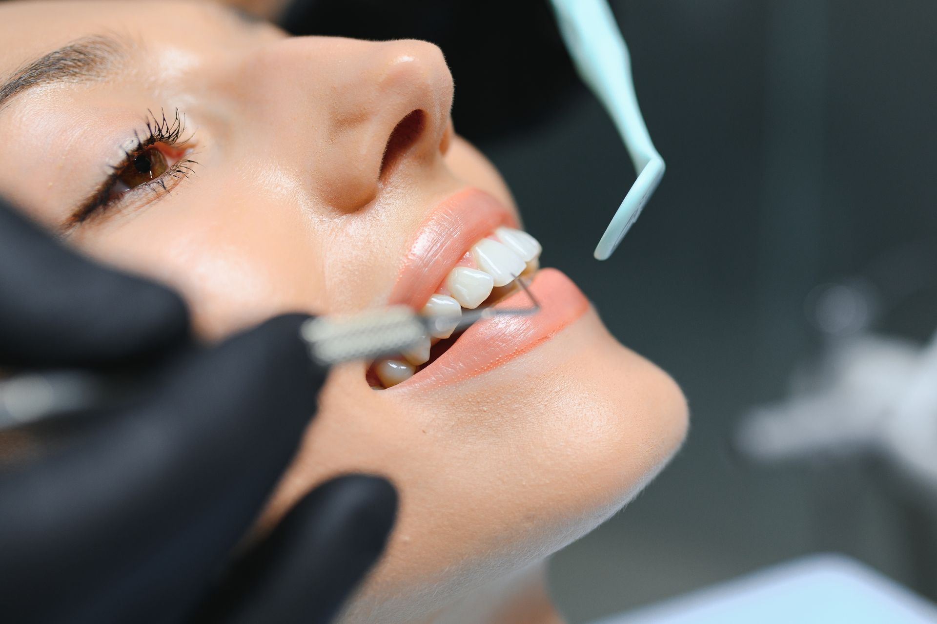 A dental professional in black gloves uses tools to examine a patient’s teeth during a dental appointment.