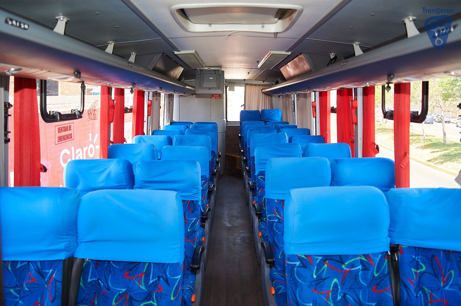 Exterior del aeropuerto con vehículos estacionados frente a un edificio. Montañas y cielo azul al fondo.