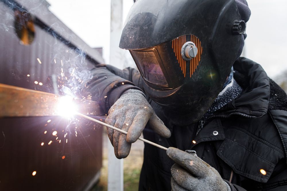 A man wearing a welding helmet is welding a piece of metal.