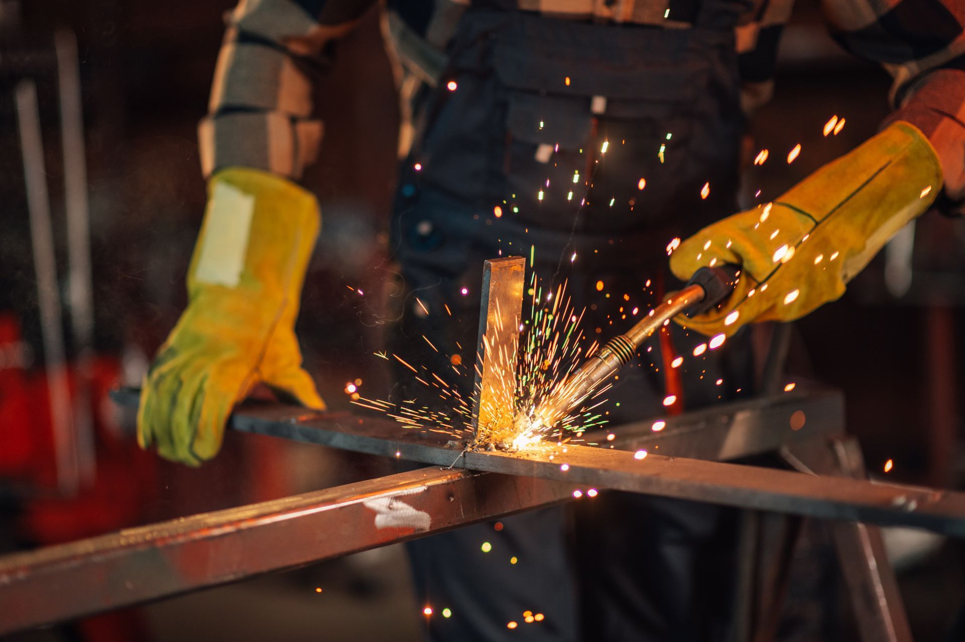 A man wearing yellow gloves is welding a piece of metal.