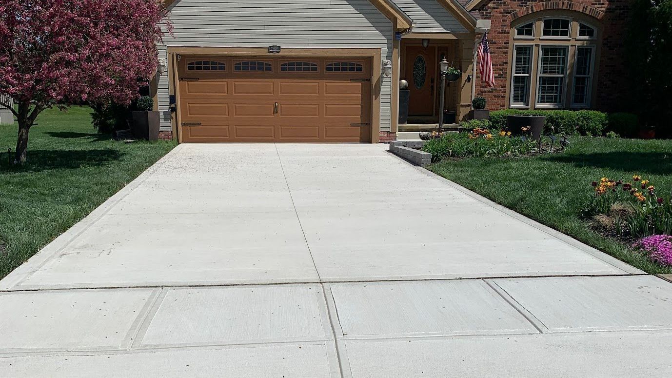 Concrete driveway leading to a house with brown garage door and landscaping on either side.