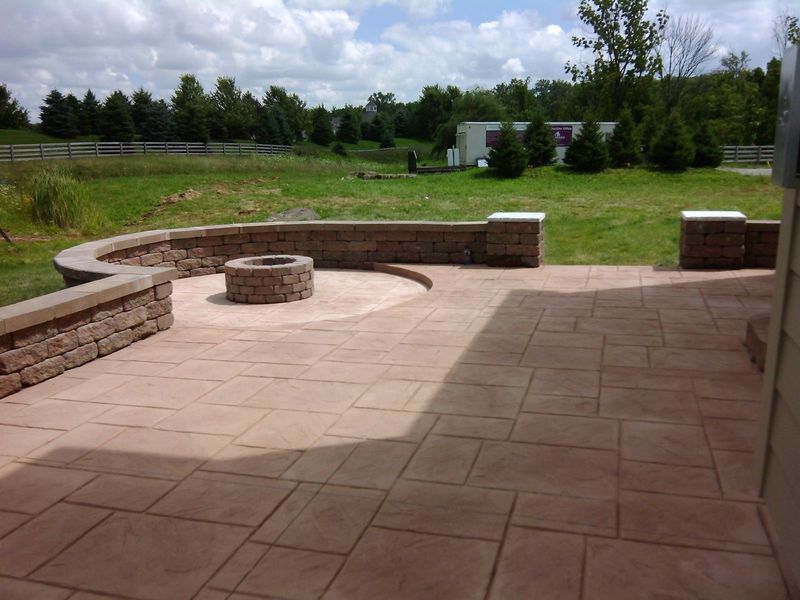 Outdoor patio with a stone fire pit, surrounded by a low brick wall and stamped concrete.