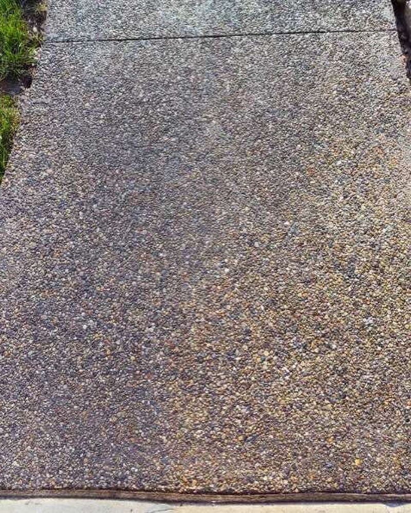 Concrete walkway with exposed aggregate surface, brown and gray hues, bordered by grass.