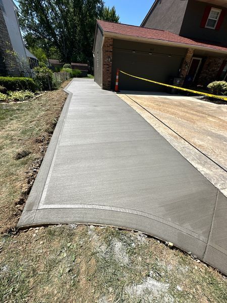 Newly poured concrete driveway with a curved border, next to a grassy area and house.