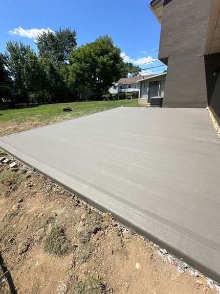 Newly poured concrete patio next to a light brown stucco house; sunny day.