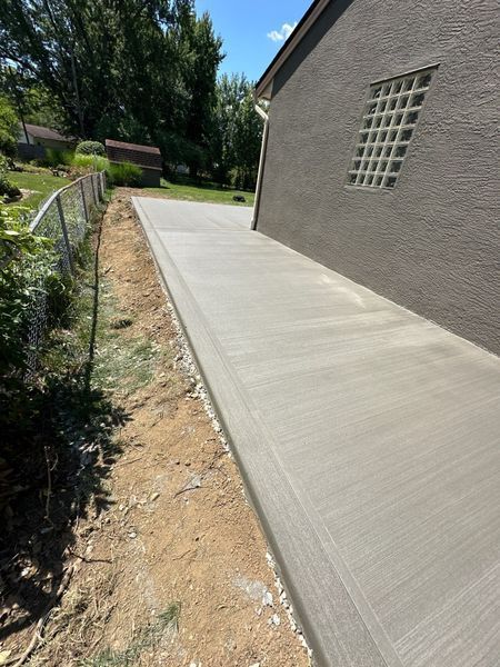 Newly poured concrete walkway next to a tan house with a small glass block window.