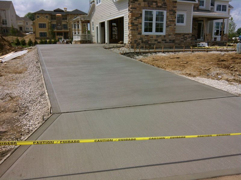 Newly poured concrete driveway with caution tape in front of a house under construction.