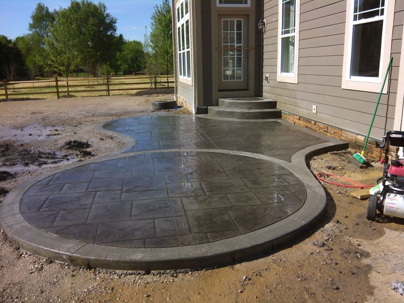 Newly poured, stamped concrete patio with curved edges, next to a house with steps.