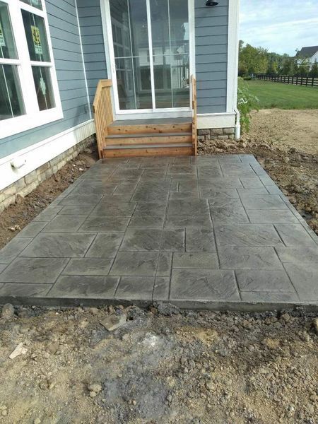 Concrete patio with stone pattern outside a house with wooden stairs and sliding glass door.