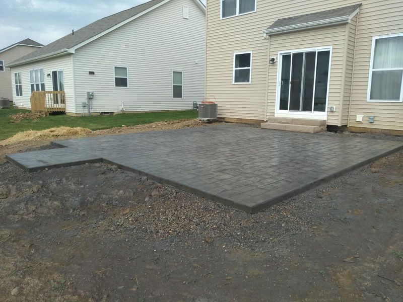 Newly constructed gray concrete patio outside a beige house.