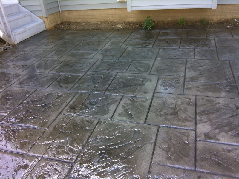 Stamped concrete patio with dark gray rectangular and square stone pattern.