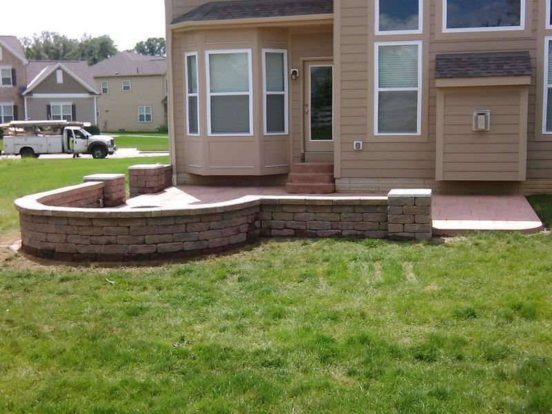 A brick patio with a low curved wall and square pillars in front of a house with a bay window.