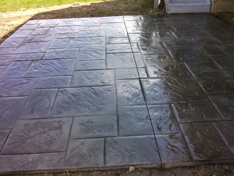 Dark gray stamped concrete patio with wet appearance.