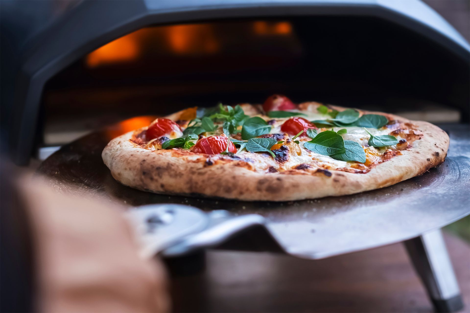 Pizza baking in a wood-fired oven, topped with basil and red peppers.