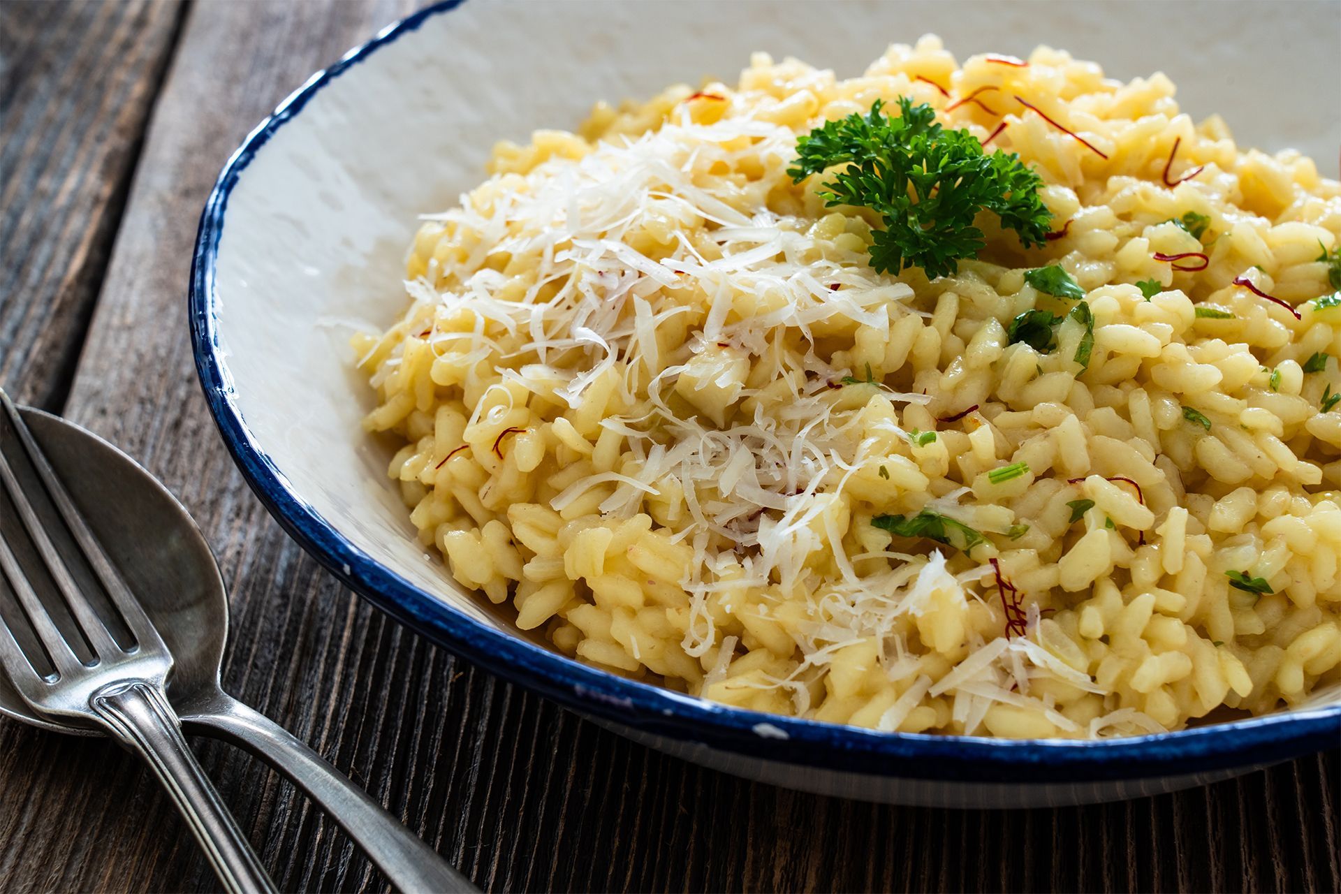 Plate of risotto with grated cheese and parsley garnish on a table with fork and spoon.