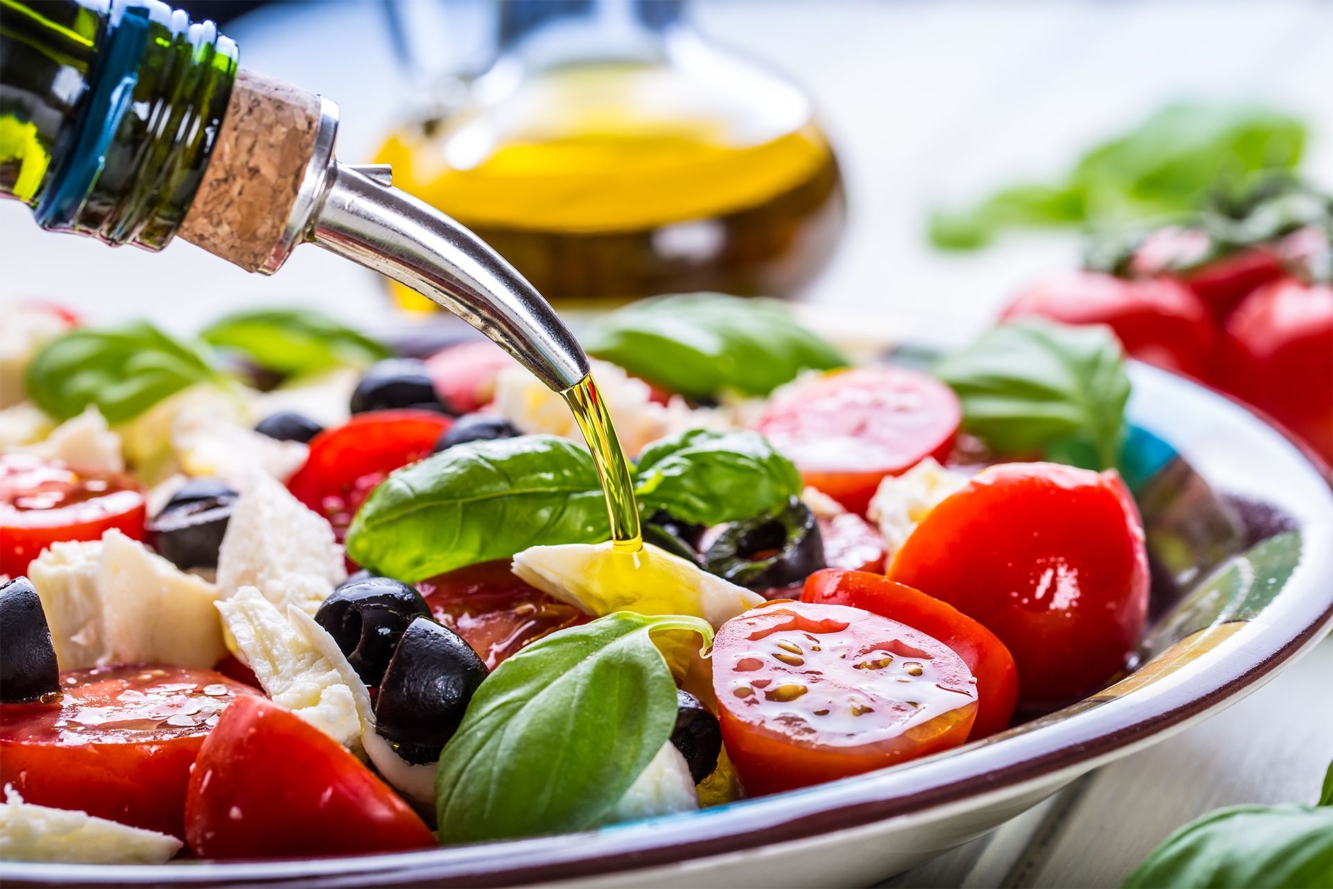 Olive oil being poured over a colorful salad with tomatoes, olives, basil, and sliced radishes. Olive oil being poured over a colorful salad with tomatoes, olives, basil, and sliced radishes.