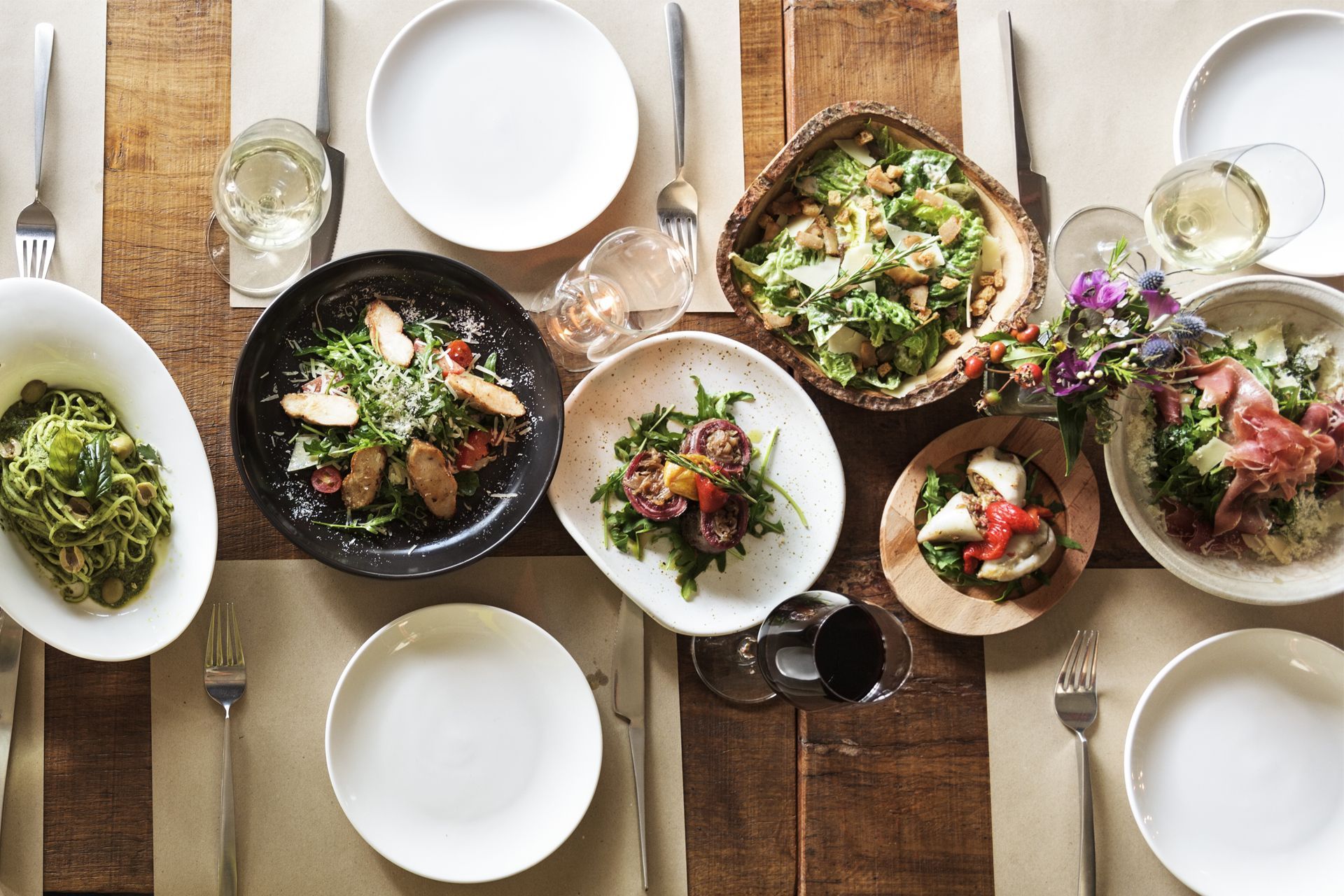 Overhead view of a rustic table set with assorted salads, plates, glasses, and silverware.