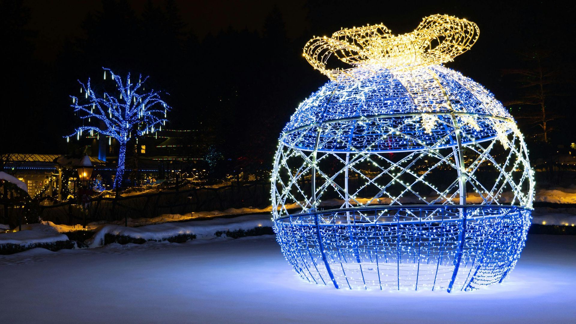 A large christmas ornament with a bow is sitting in the snow.