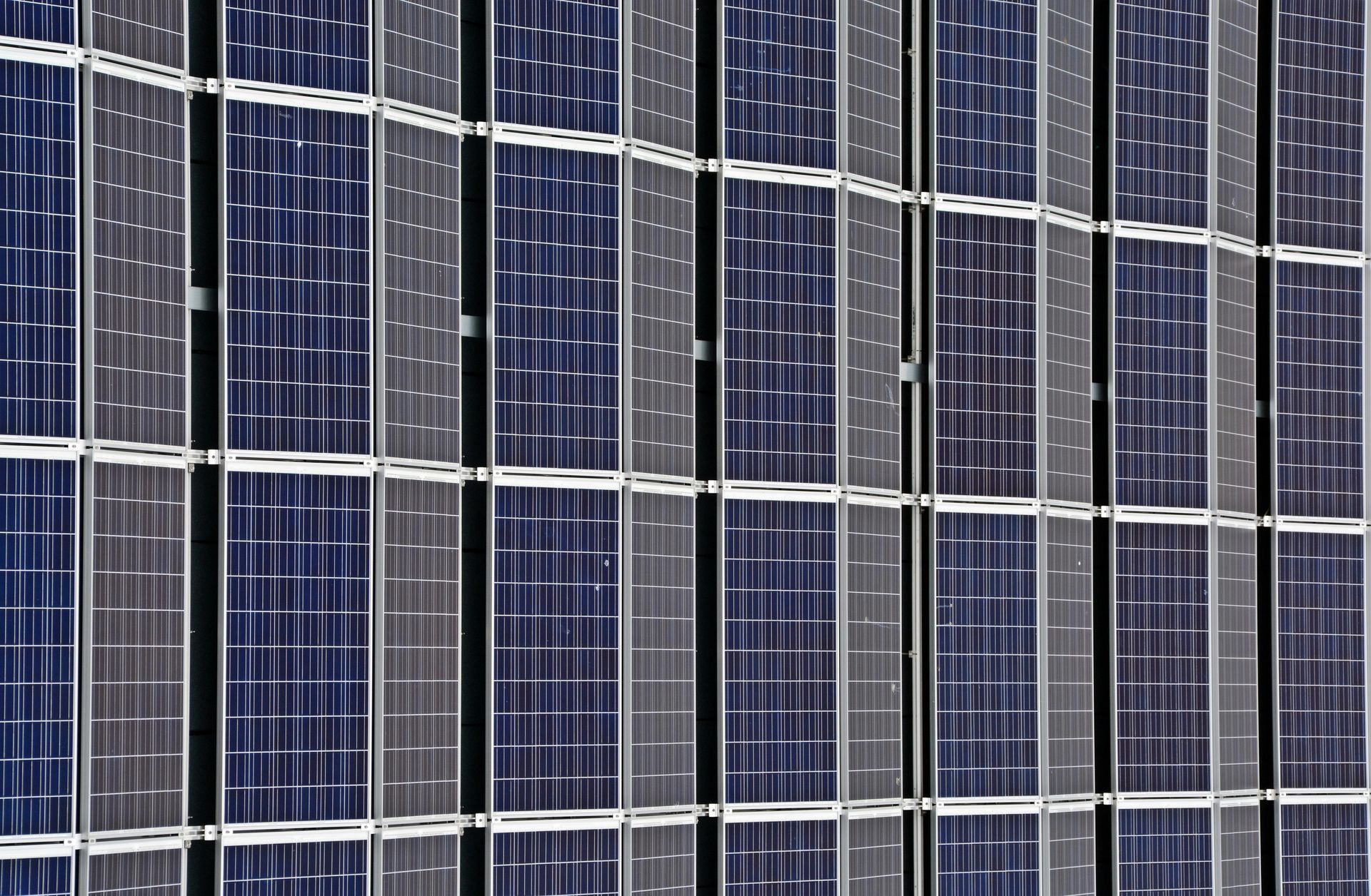 Close-up of a building facade covered in a grid of rectangular solar panels, reflecting sunlight with a blue hue.