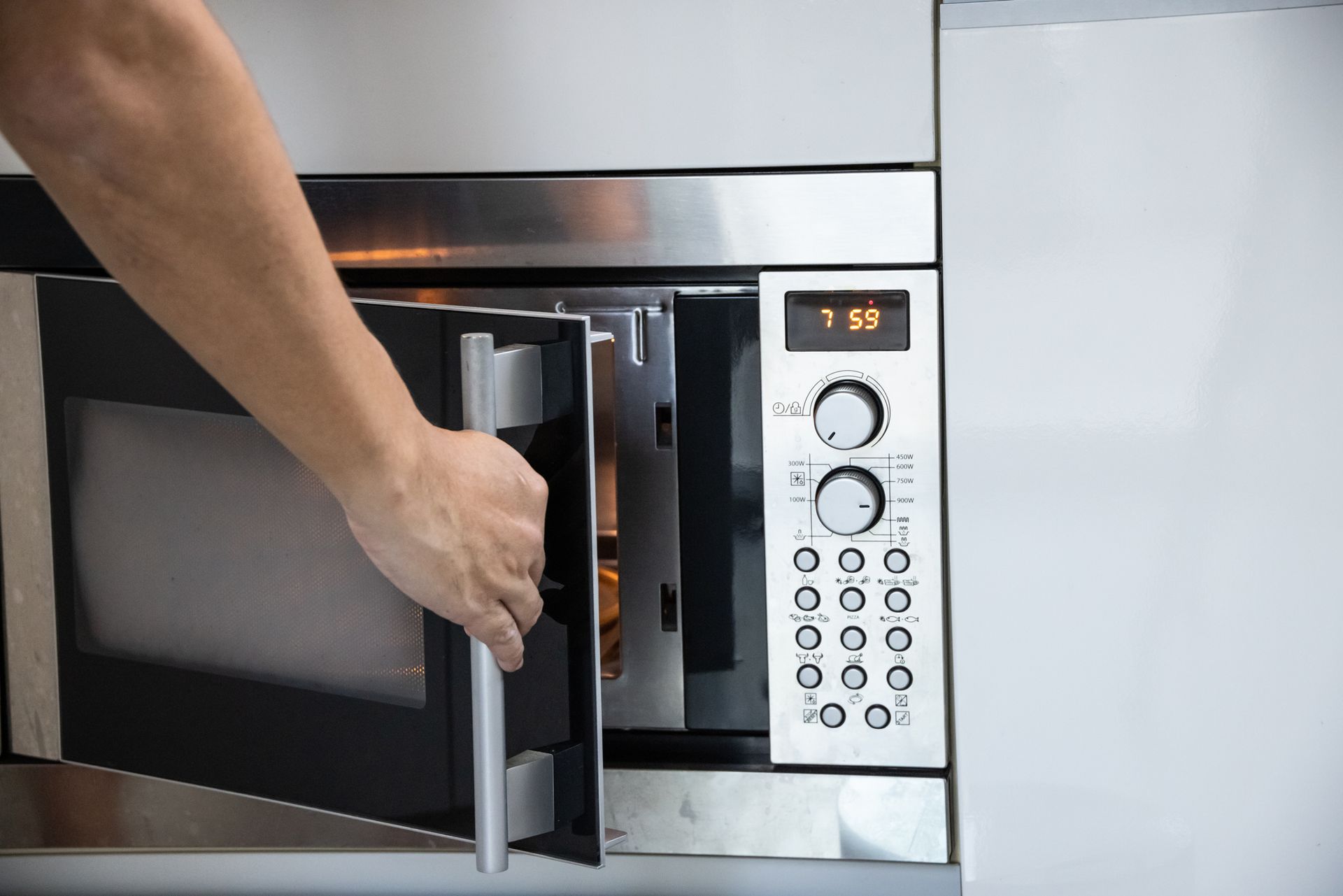 Hand opening a microwave oven door in a kitchen.