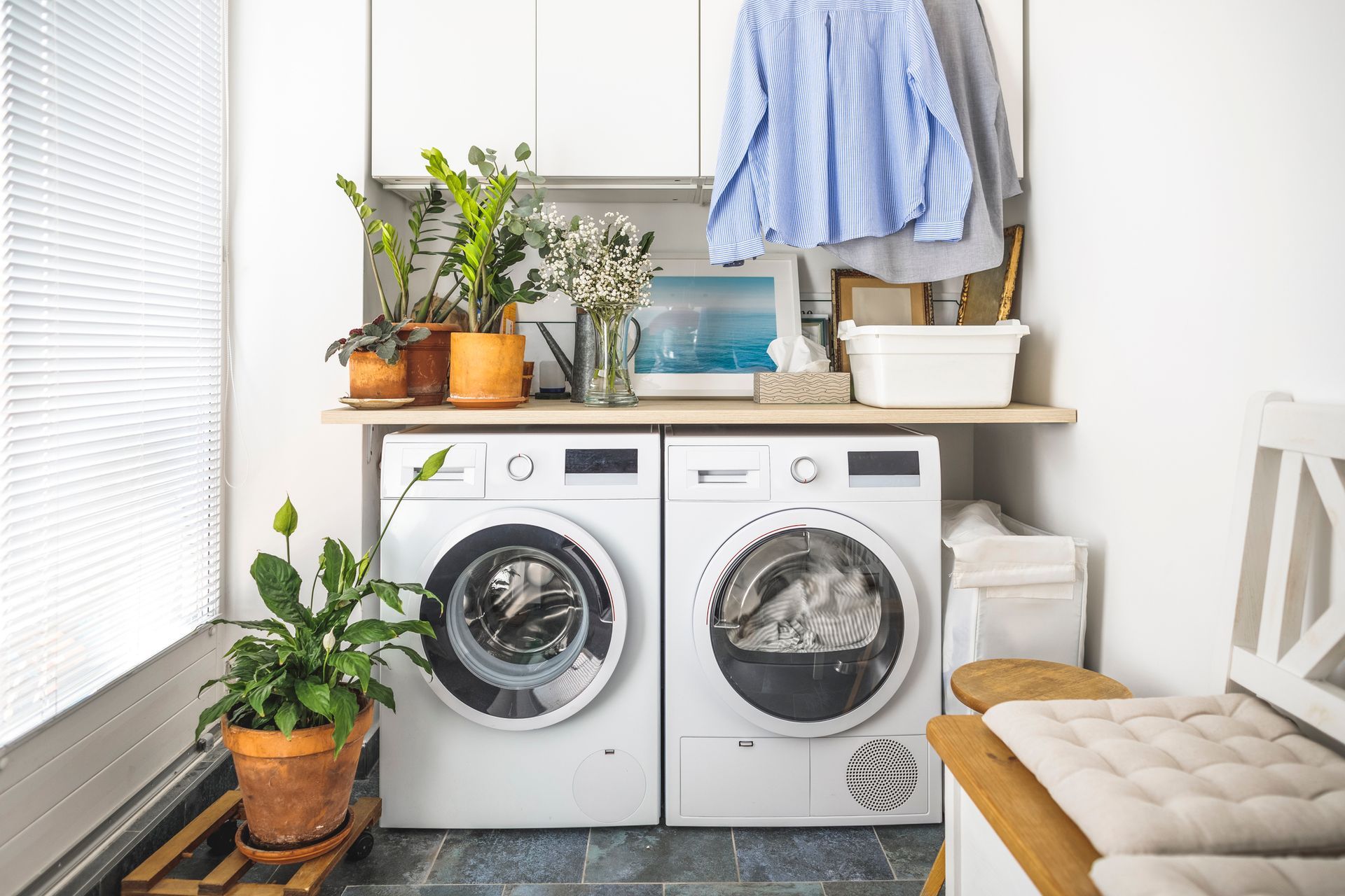 A laundry room with a washer, dryer, plants, and a clothes rack.