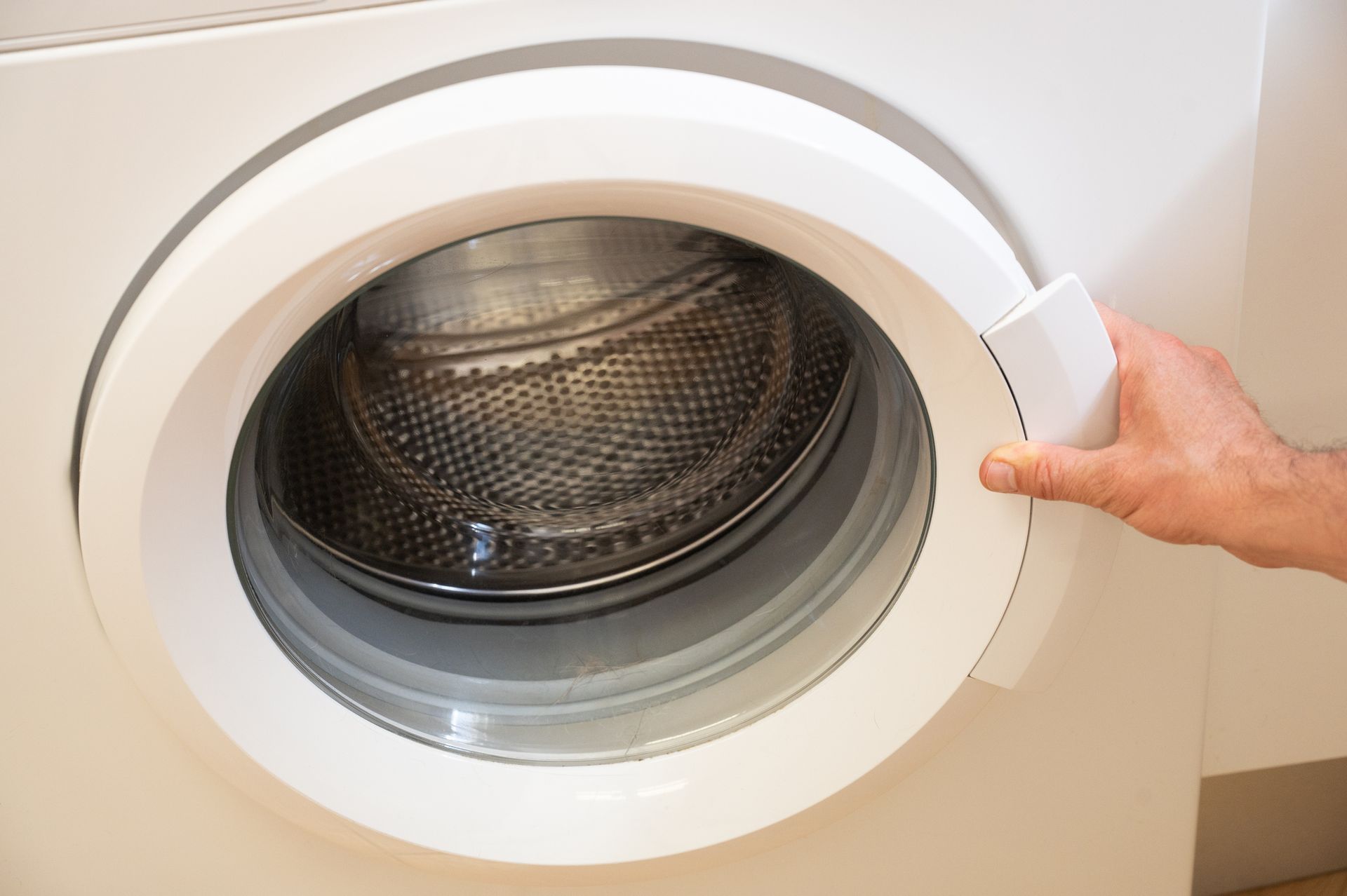 Person opening a white washing machine door.