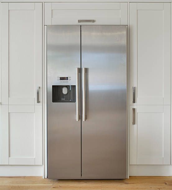 Stainless steel side-by-side refrigerator flanked by white cabinets.
