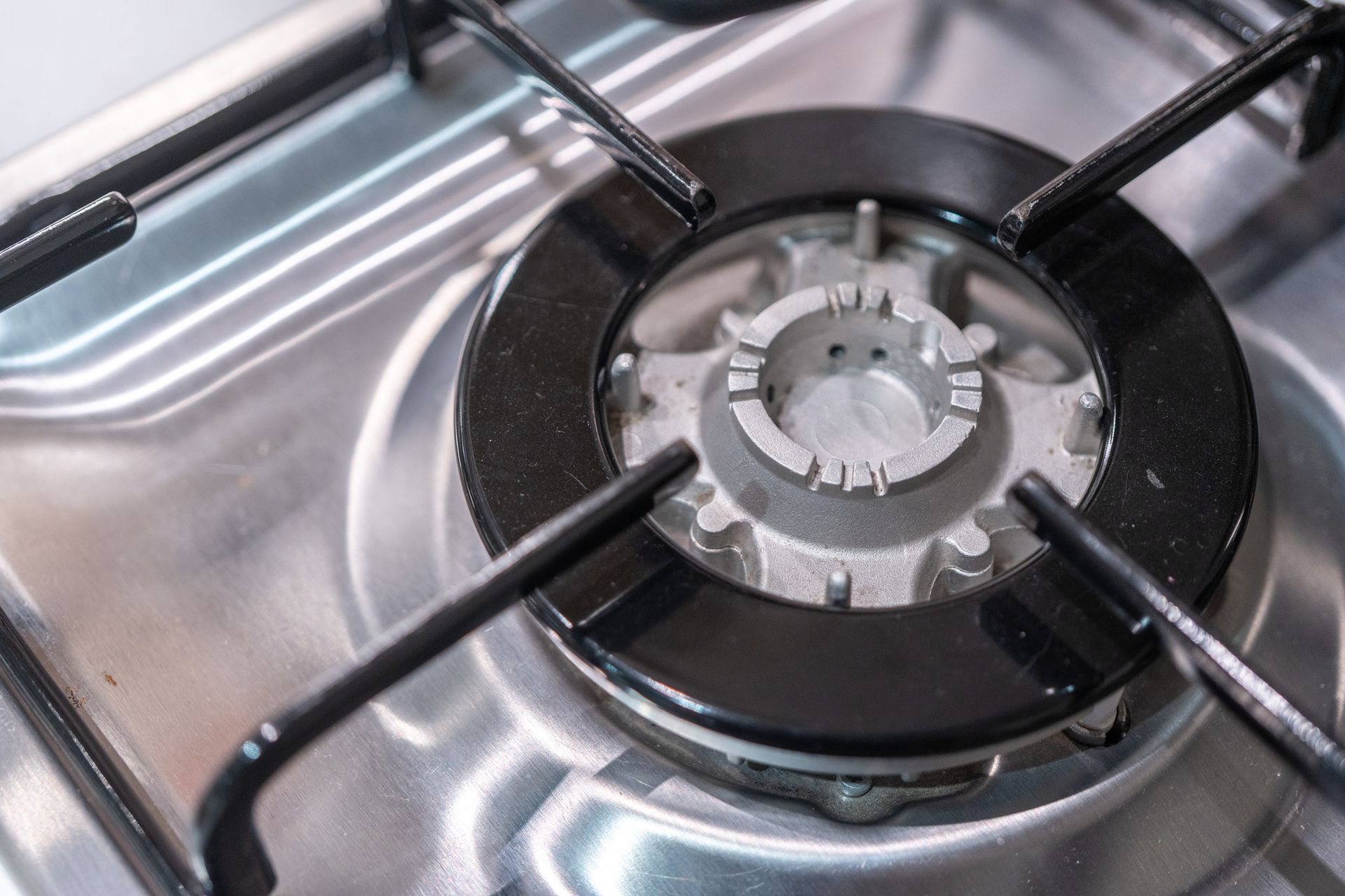 Close-up of a gas stove burner with black metal grate on a stainless steel surface.