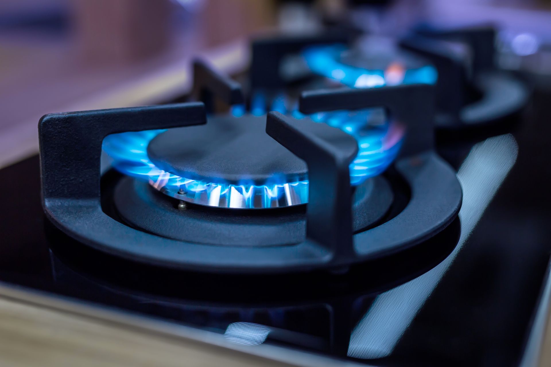 Close-up of a gas stove burner with blue flames lit.