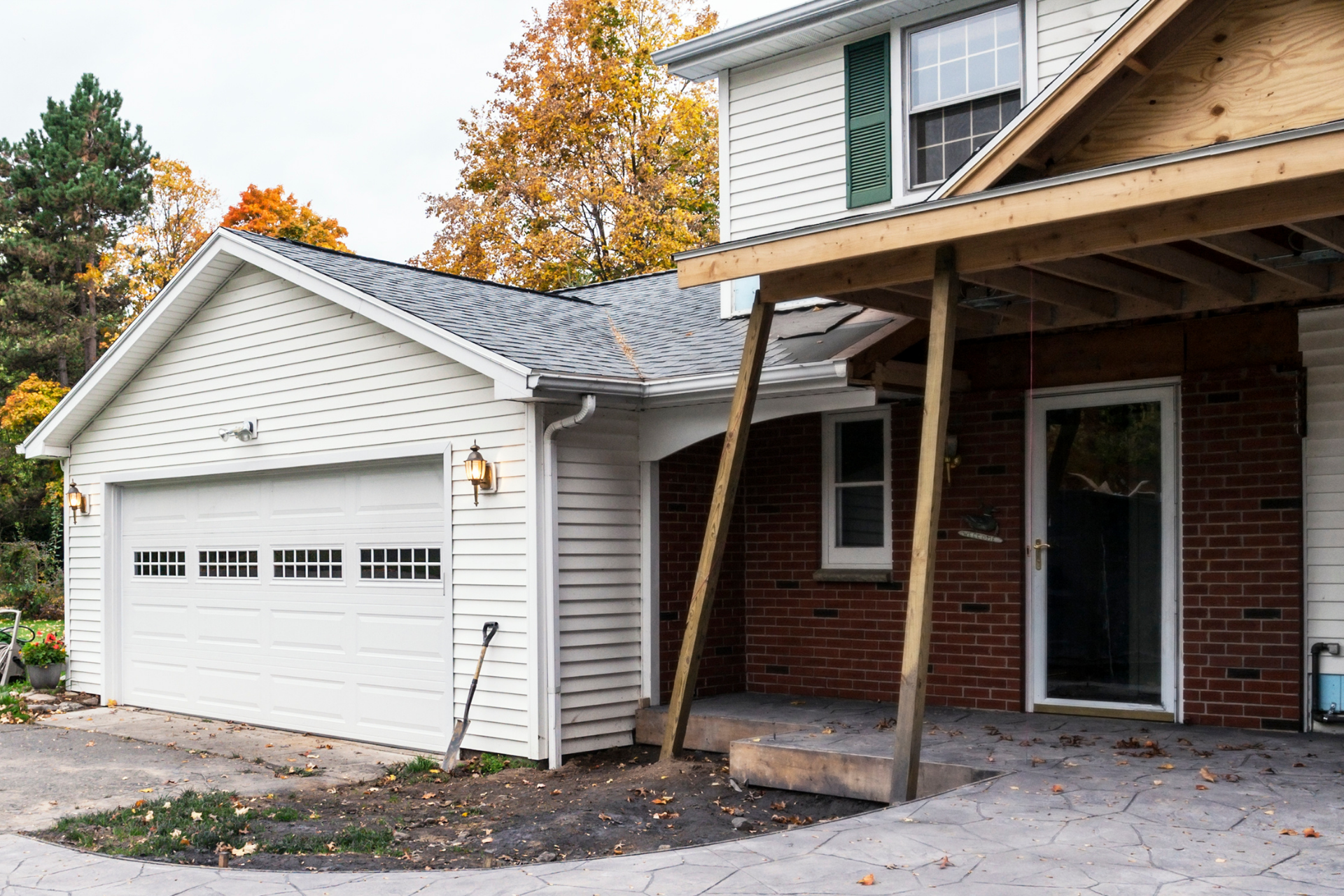 House exterior with white garage, brick porch, and a damaged carport roof supported by wooden posts