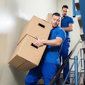 Two Men Carrying Boxes Up A Set Of Stairs