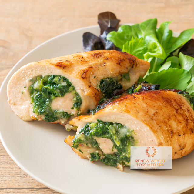 Renew Weight Loss and Med Spa's Spinach and Feta Stuffed Chicken Breast on a white plate, garnished with oregano and fresh spinach leaves, in a modern kitchen setting.