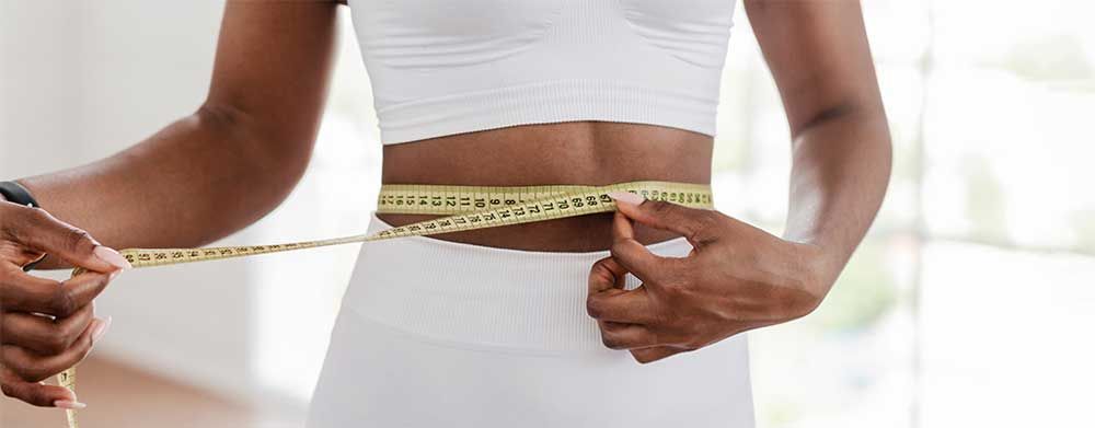 A woman is measuring her waist with a tape measure.