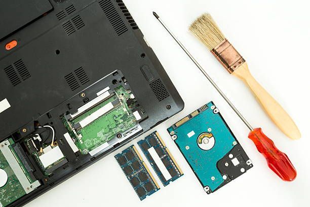 A laptop is being repaired with a screwdriver and a brush.