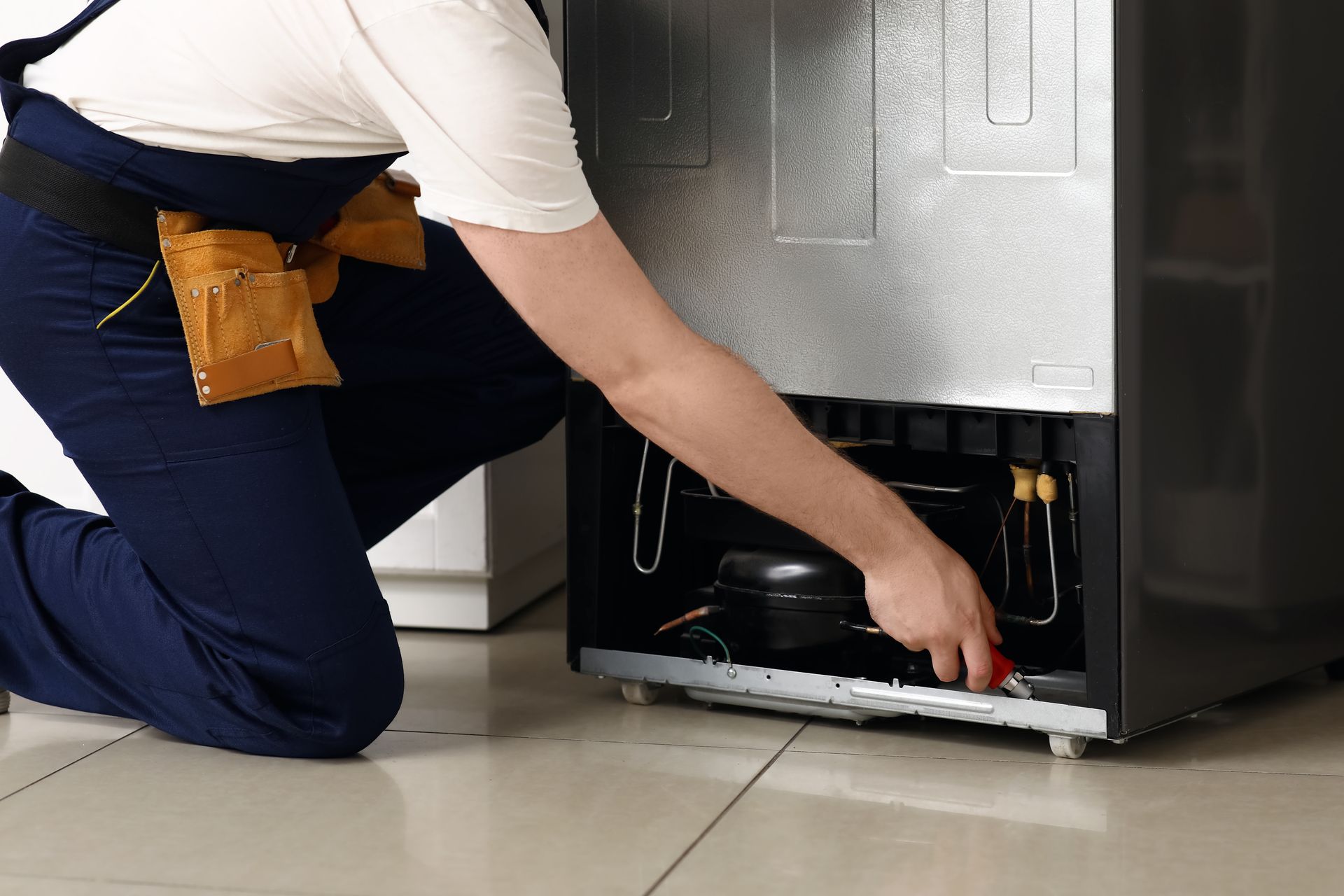 A man is kneeling down to fix a refrigerator.