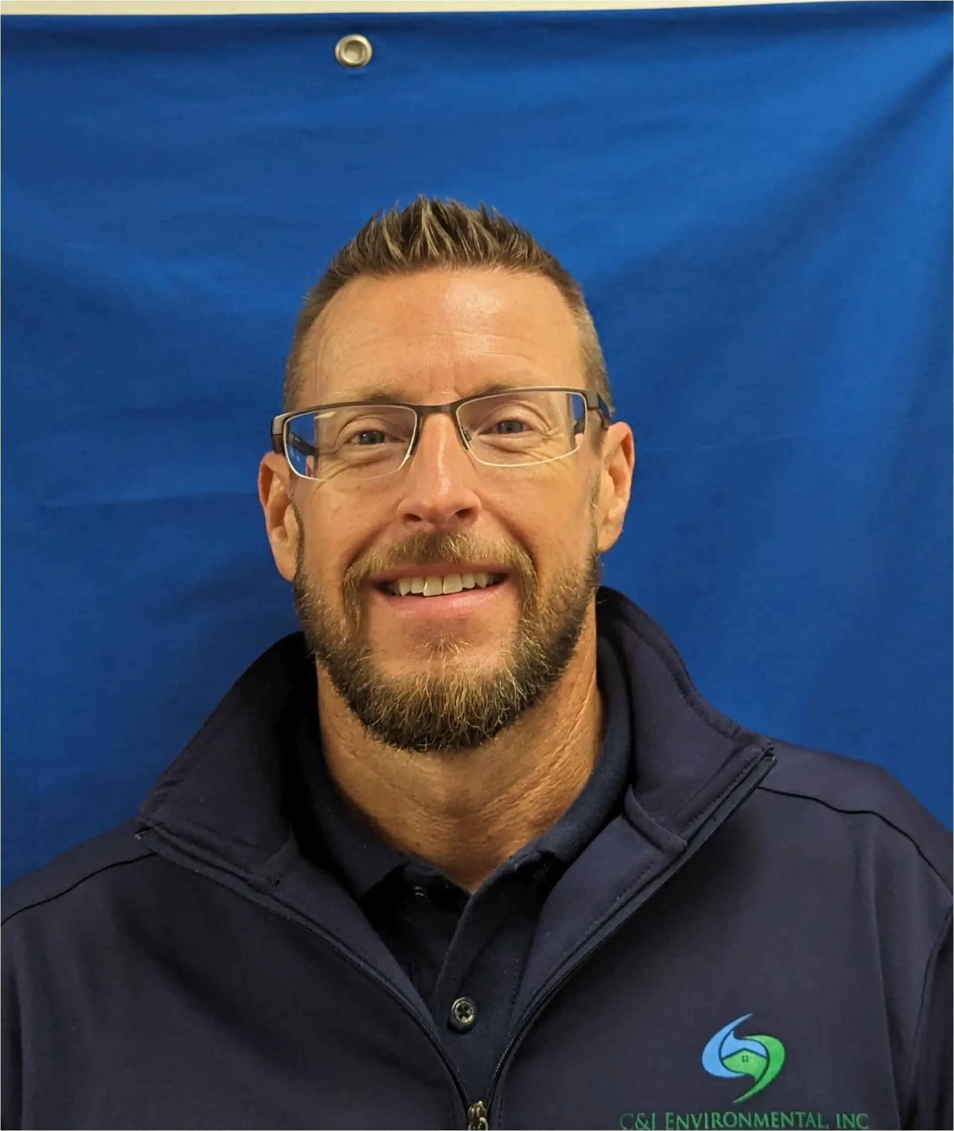 A man with glasses and a beard is smiling in front of a blue background