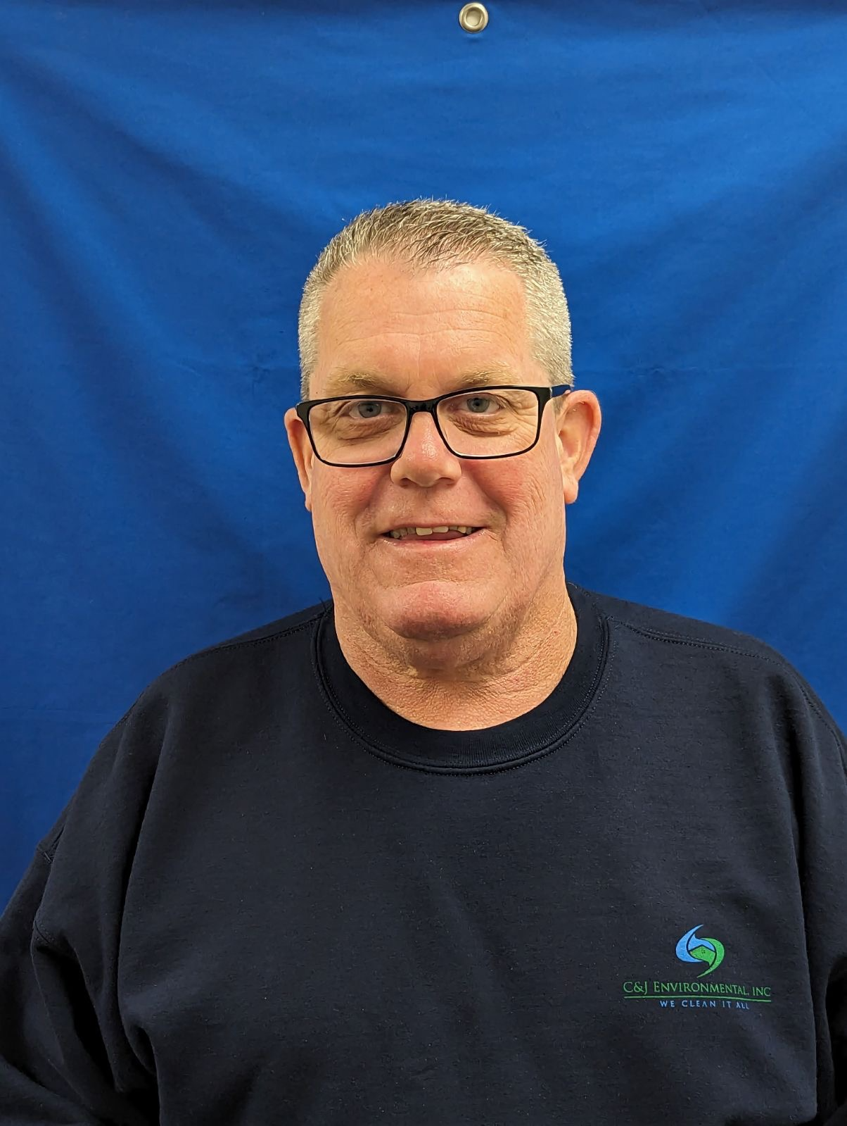 A man wearing glasses and a blue shirt is standing in front of a blue background.