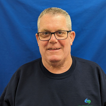 A man wearing glasses and a blue shirt is smiling for the camera.