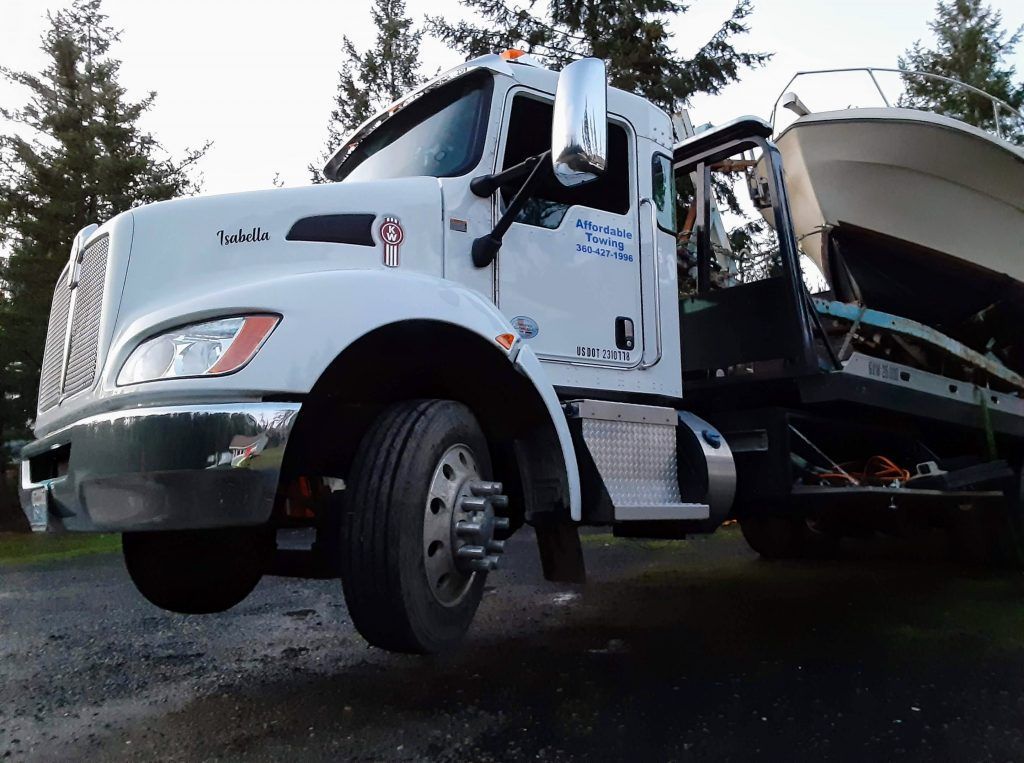 A white tow truck with a boat on the back of it