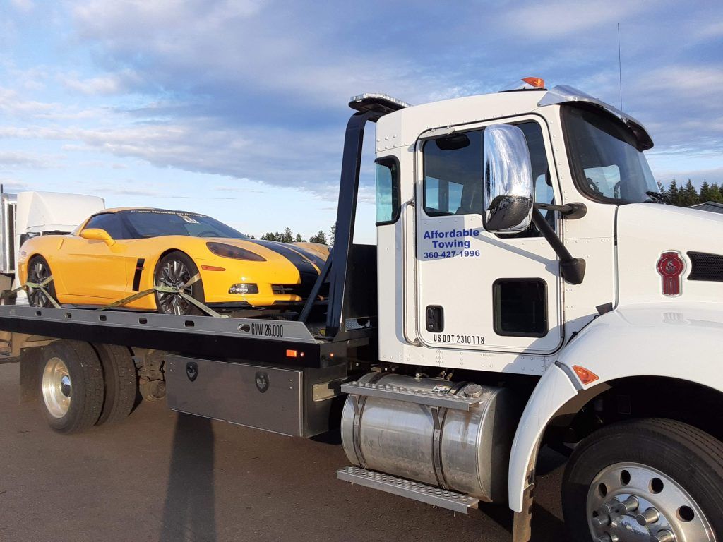 A tow truck is carrying a yellow sports car on the back of it.