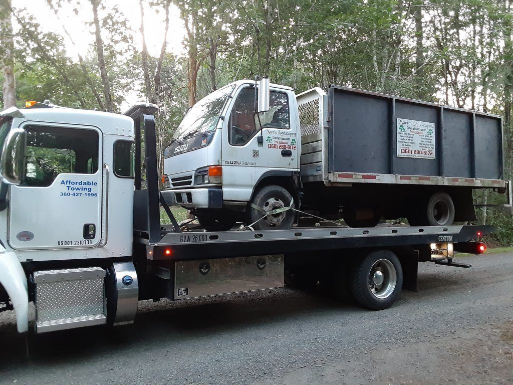 A white tow truck is carrying a dump truck