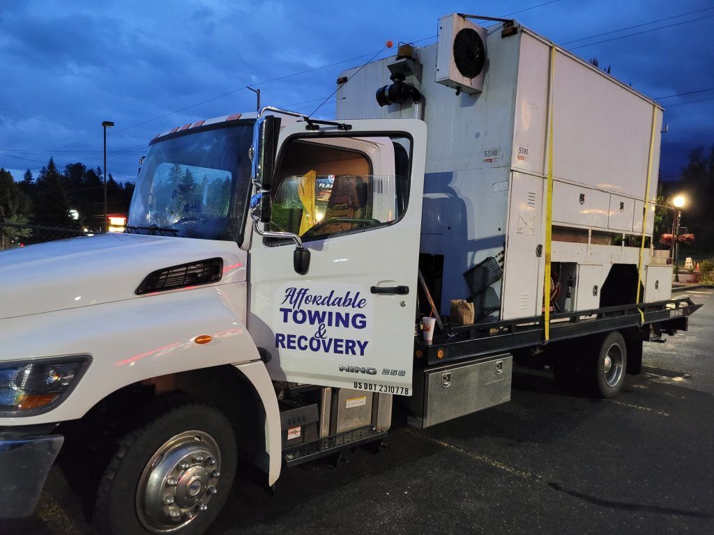 A white towing truck is parked in a parking lot at night.