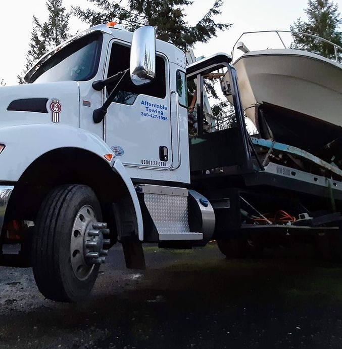 A white tow truck with a boat on the back of it