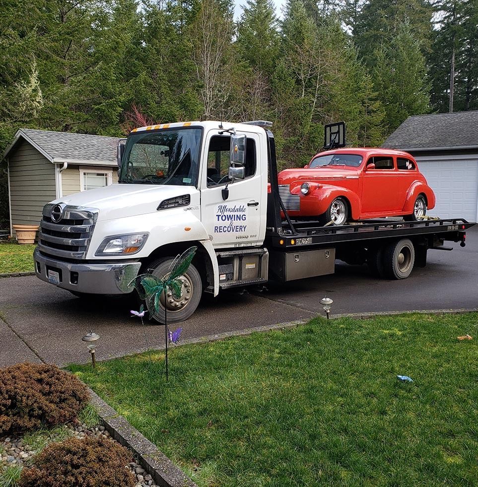 A tow truck is towing a red car in a driveway.